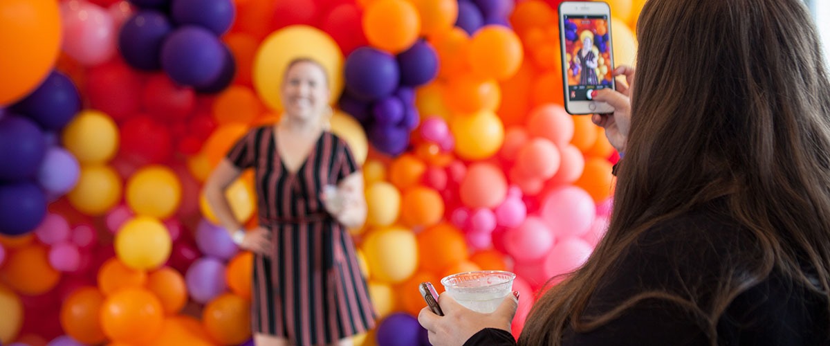 a woman takes a picture of another young woman standing in front of balloons at Balcony Bar
