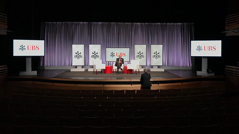 A speaker sits on the stage as guests arrive for a presentation from Swiss investment bank UBS.