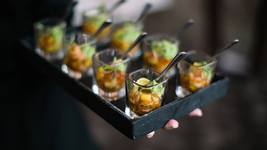 Close up of appetizers in small glasses on a black tray.